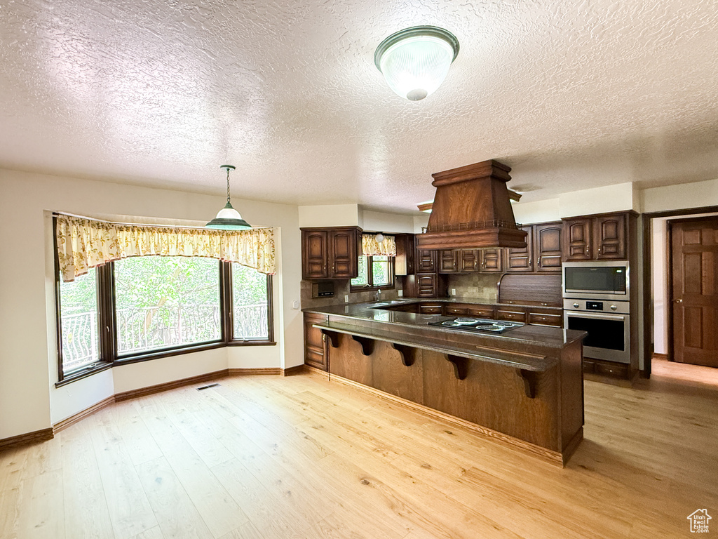 Kitchen featuring appliances with stainless steel finishes, custom exhaust hood, dark countertops, a breakfast bar area, and a textured ceiling