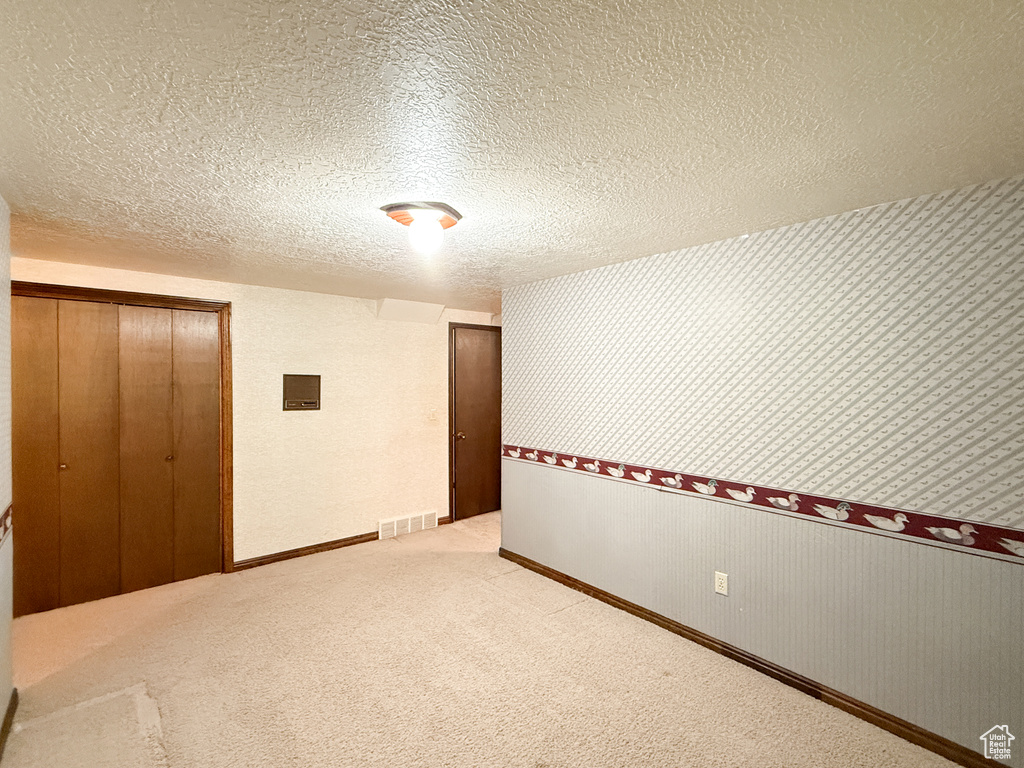 Carpeted spare room featuring wallpapered walls, electric panel, a textured ceiling, and baseboards