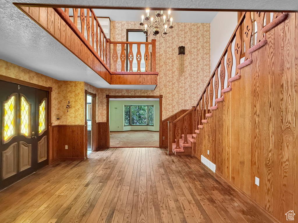 Foyer with stairway, hardwood / wood-style flooring, wallpapered walls, a wainscoted wall, and a chandelier