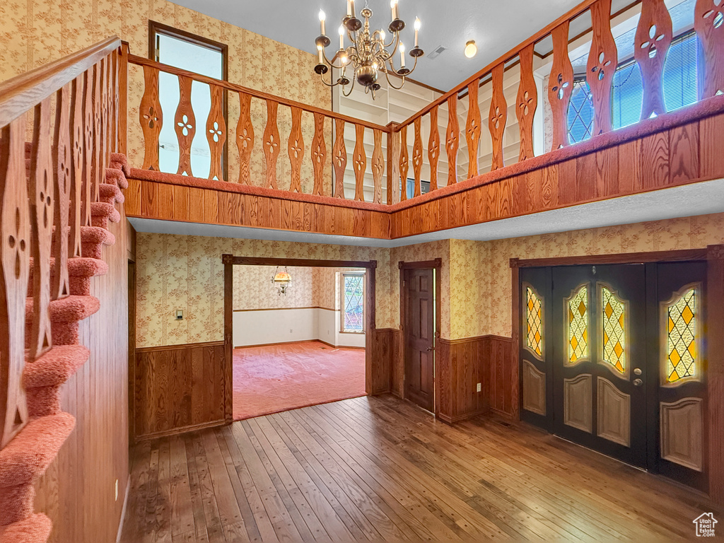 Unfurnished living room with wallpapered walls, wainscoting, wood-type flooring, a high ceiling, and a chandelier