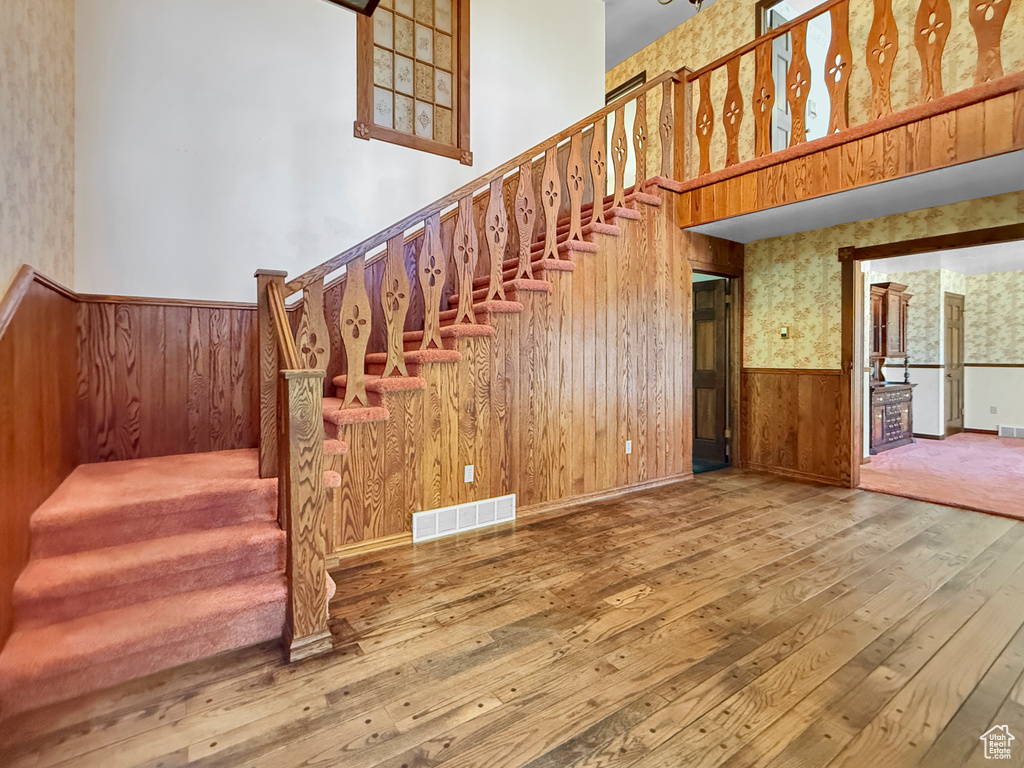 Staircase with hardwood / wood-style floors, a wainscoted wall, wallpapered walls, wood walls, and a towering ceiling