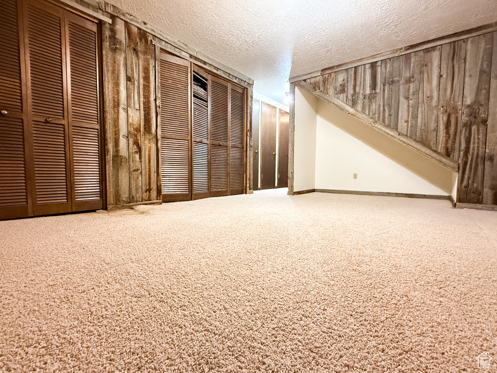 Basement featuring a textured ceiling, wooden walls, carpet, and baseboards