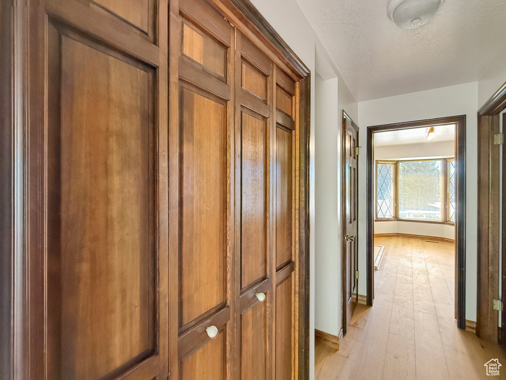 Hall with baseboards, light wood-style floors, and a textured ceiling