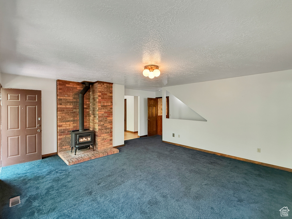 Unfurnished living room with a wood stove, a textured ceiling, dark colored carpet, and baseboards