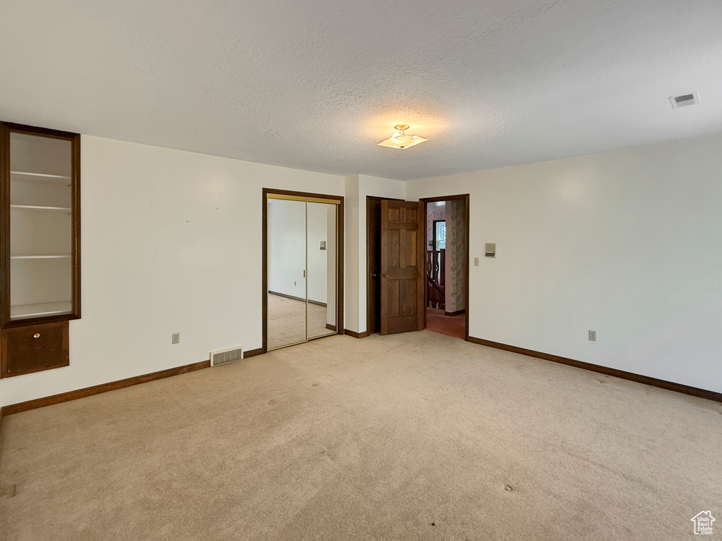 Empty room with light carpet, baseboards, and a textured ceiling