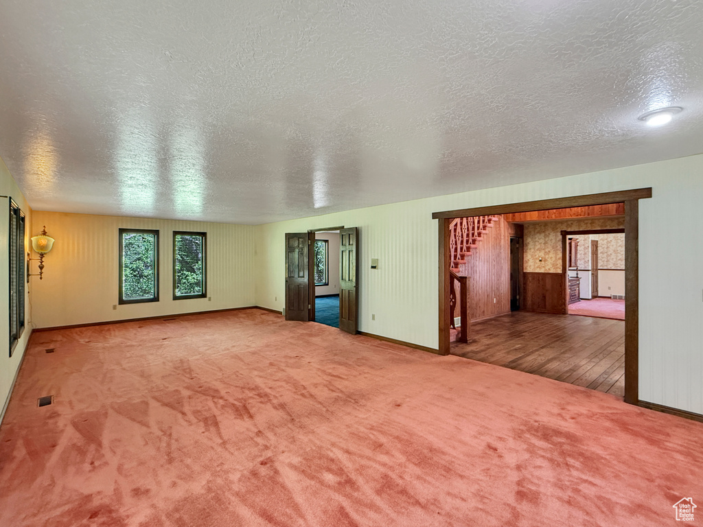 Unfurnished living room featuring a textured ceiling, carpet flooring, baseboards, and wood walls