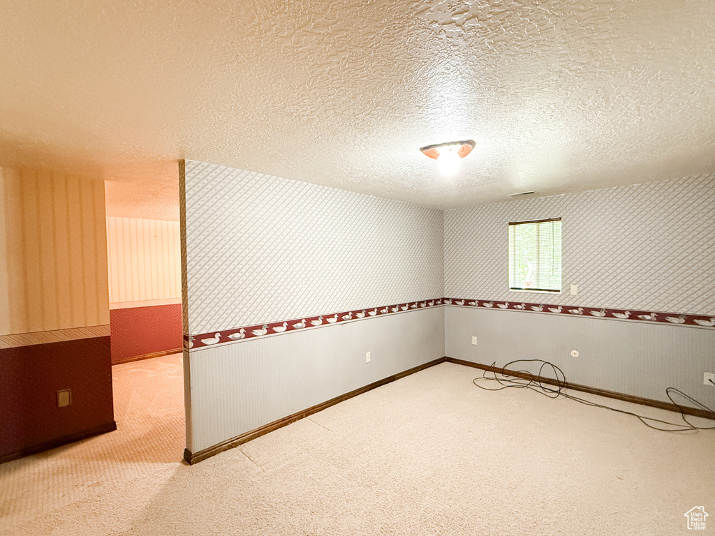 Empty room with carpet, a textured ceiling, and wallpapered walls