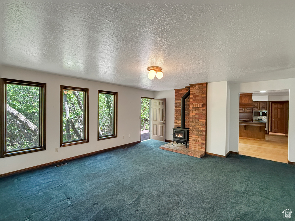 Unfurnished living room with plenty of natural light, a wood stove, carpet flooring, a textured ceiling, and baseboards