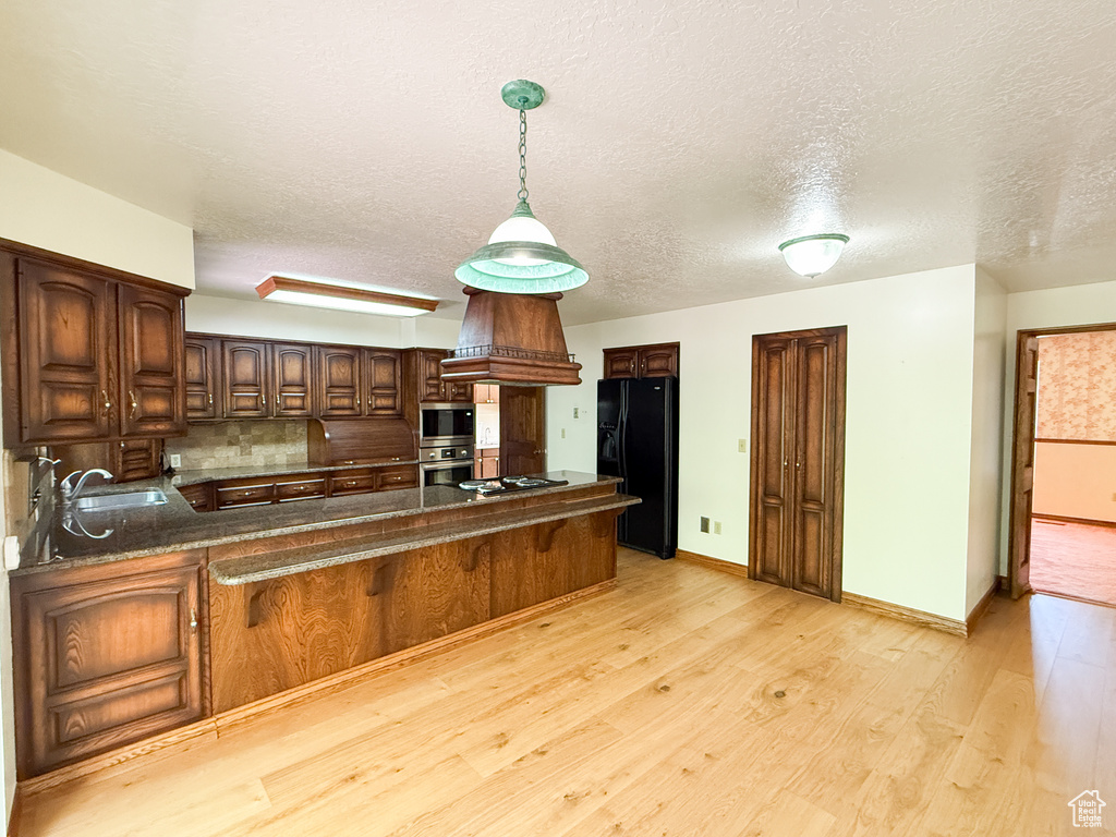 Kitchen featuring stainless steel appliances, a peninsula, a sink, a textured ceiling, and light wood-style floors