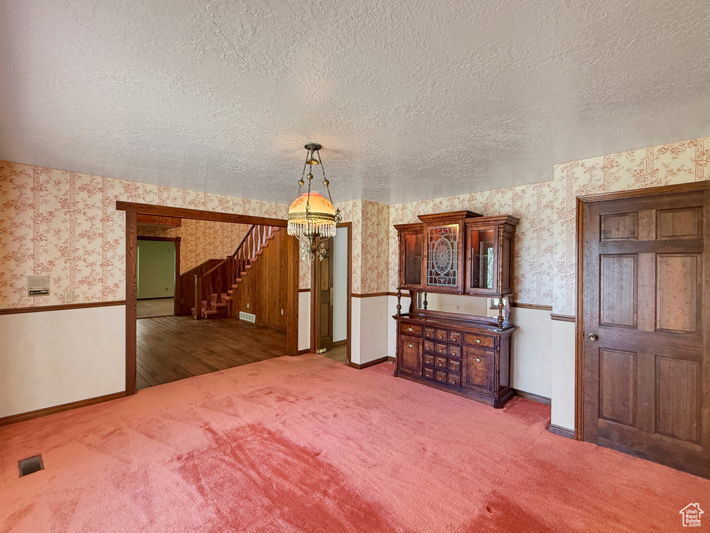 Unfurnished dining area with wallpapered walls, a chandelier, carpet flooring, a textured ceiling, and baseboards