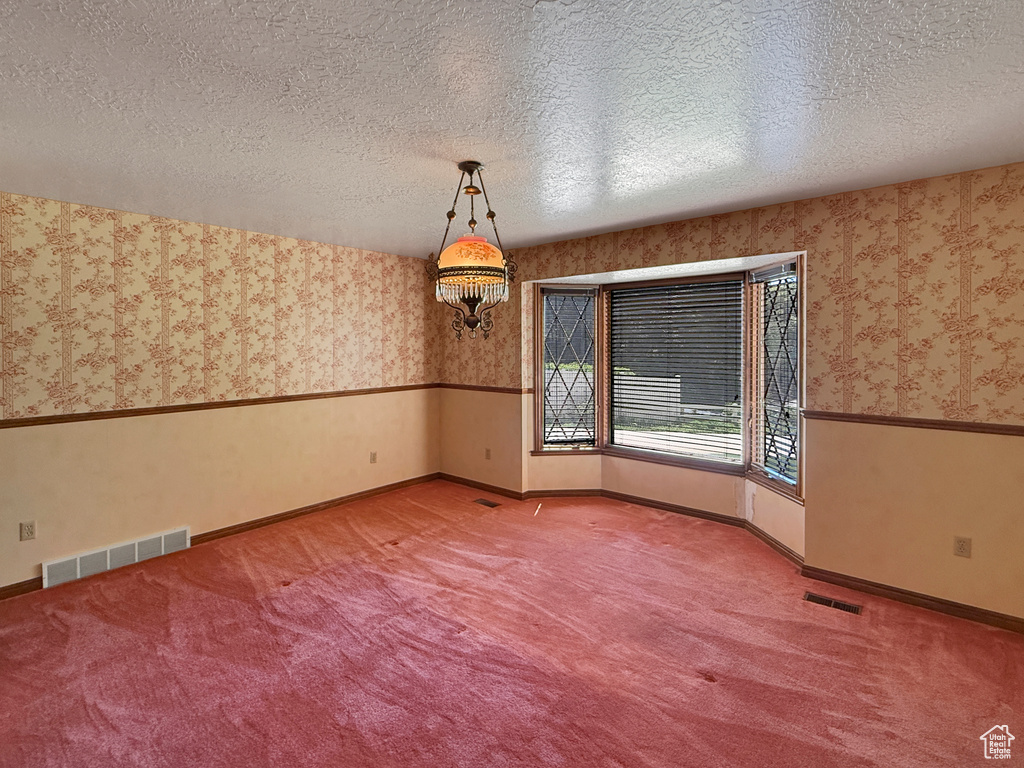 Empty room with wallpapered walls, carpet floors, baseboards, and a textured ceiling