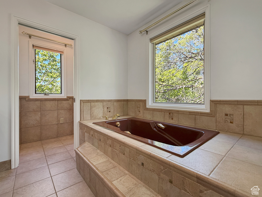 Full bathroom featuring a garden tub, a wainscoted wall, tile patterned flooring, and tile walls