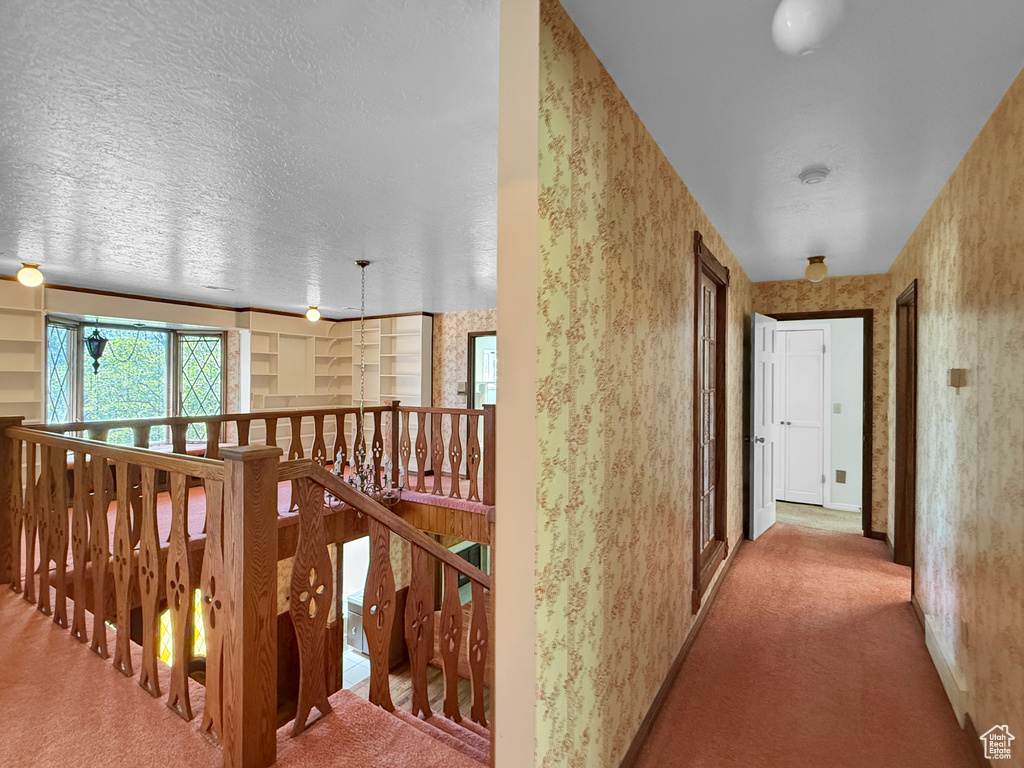 Corridor featuring an upstairs landing, carpet flooring, wallpapered walls, a textured ceiling, and baseboards