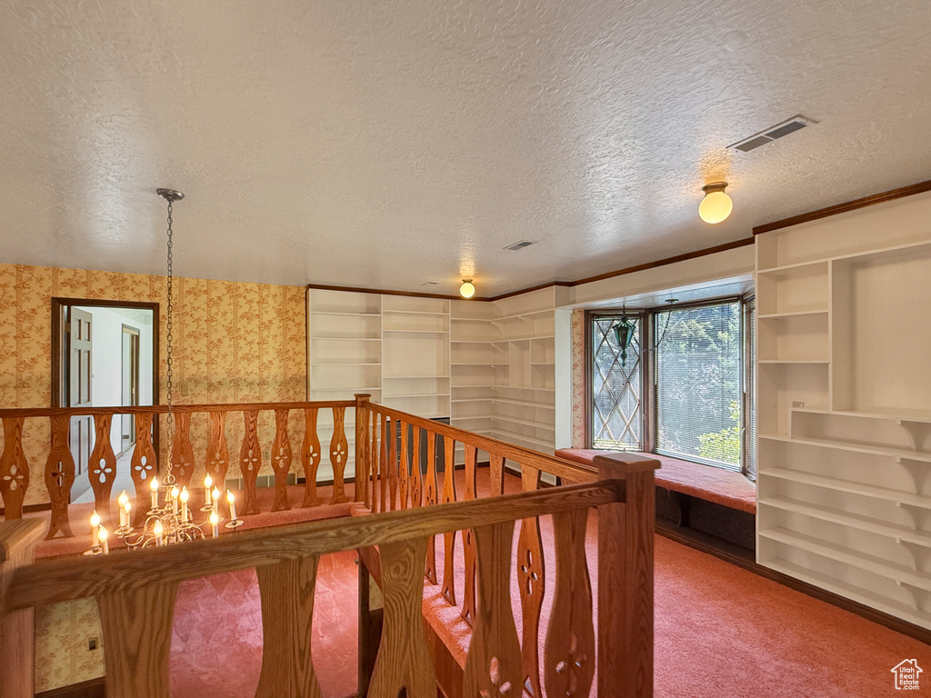 Corridor featuring a textured ceiling, carpet, wallpapered walls, and an upstairs landing
