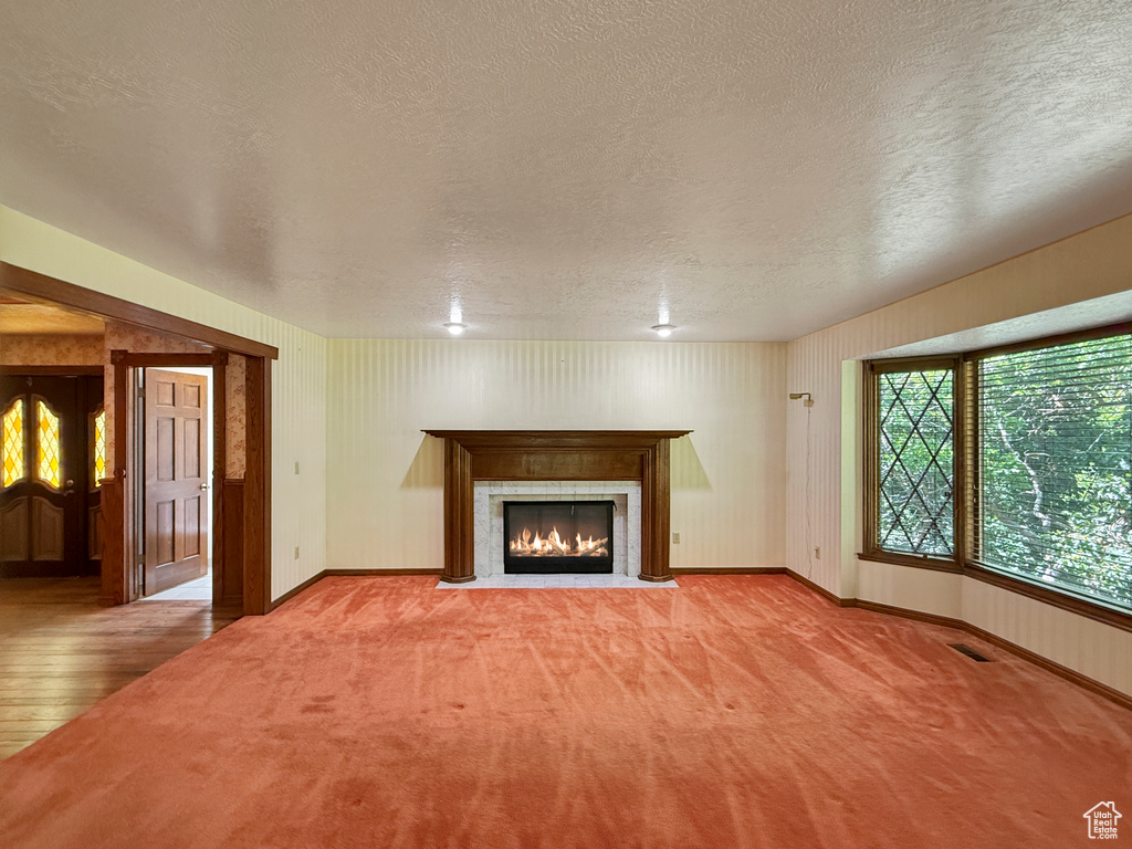 Unfurnished living room with a textured ceiling, a fireplace with flush hearth, baseboards, carpet, and wood finished floors