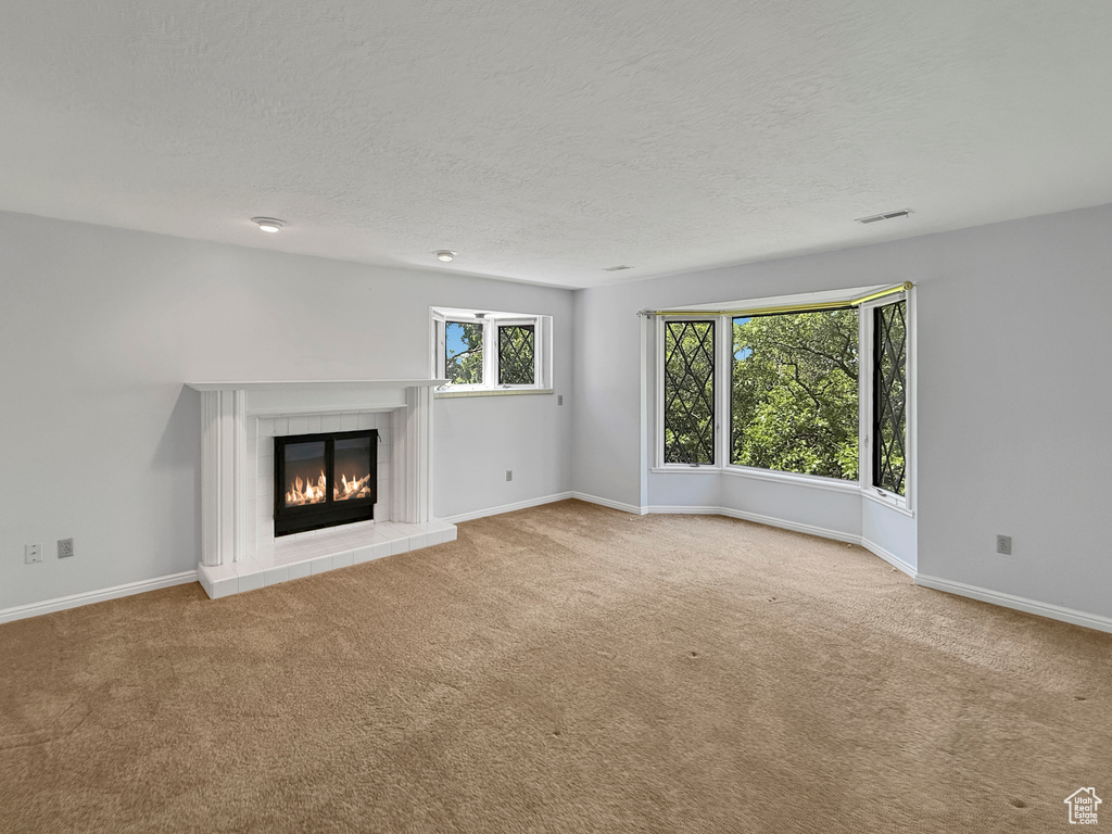 Unfurnished living room with carpet, a tile fireplace, baseboards, and a textured ceiling