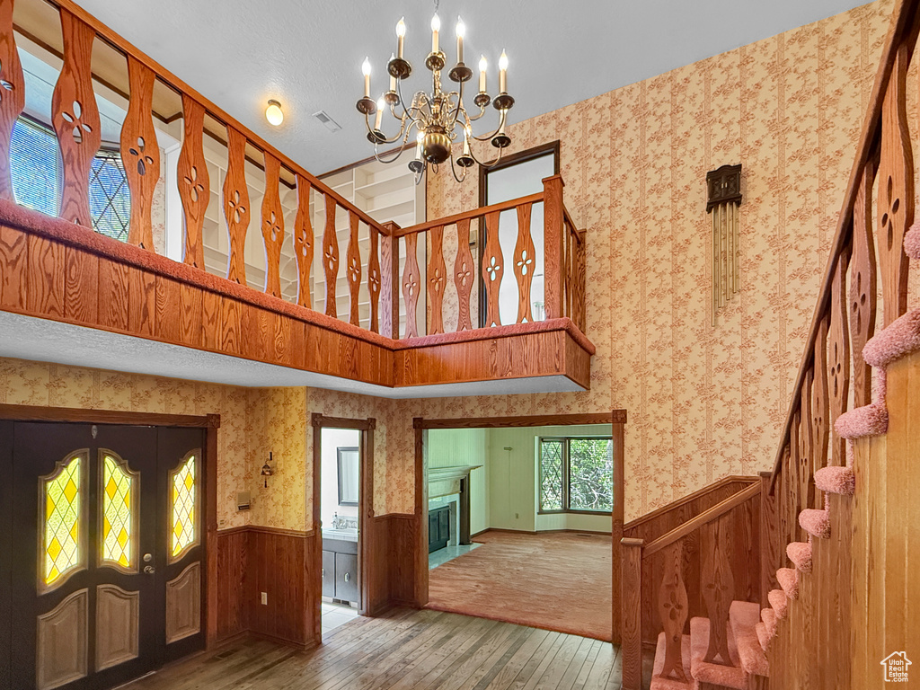 Staircase featuring hardwood / wood-style floors, wainscoting, a chandelier, french doors, and a high ceiling