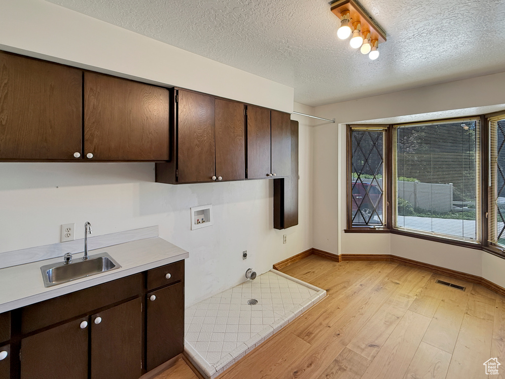 Kitchen featuring a sink, light wood-style flooring, dark brown cabinetry, light countertops, and baseboards