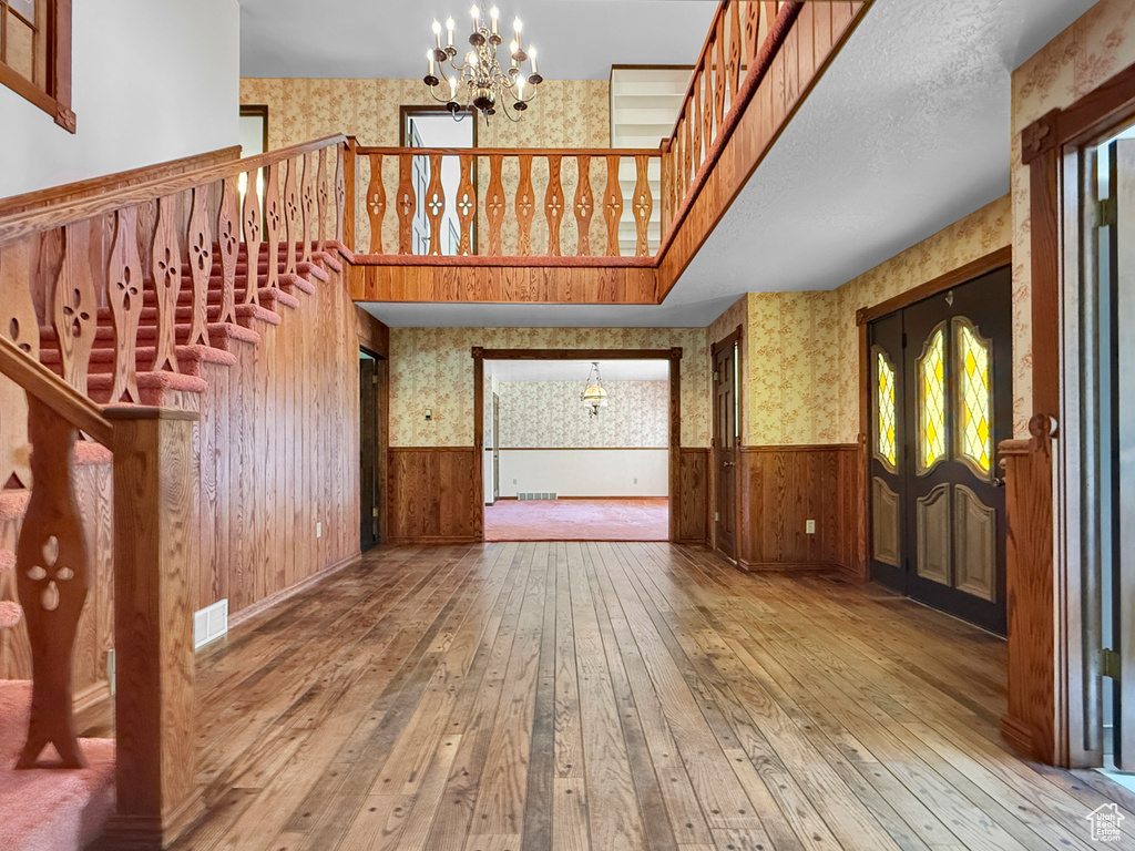 Unfurnished living room with wallpapered walls, a chandelier, wainscoting, wood-type flooring, and stairs