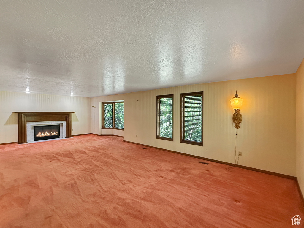 Unfurnished living room featuring a textured ceiling, carpet floors, a glass covered fireplace, and baseboards