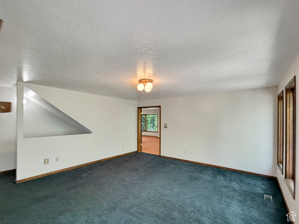 Carpeted empty room with a textured ceiling and baseboards