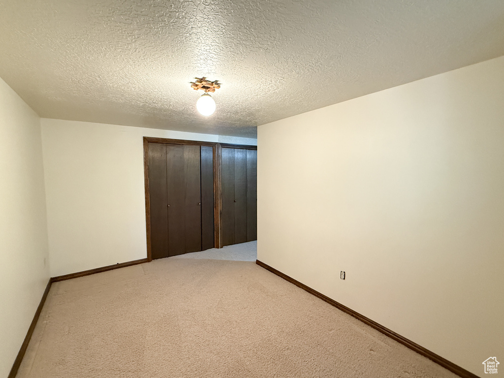 Unfurnished bedroom featuring a closet, baseboards, a textured ceiling, and light colored carpet