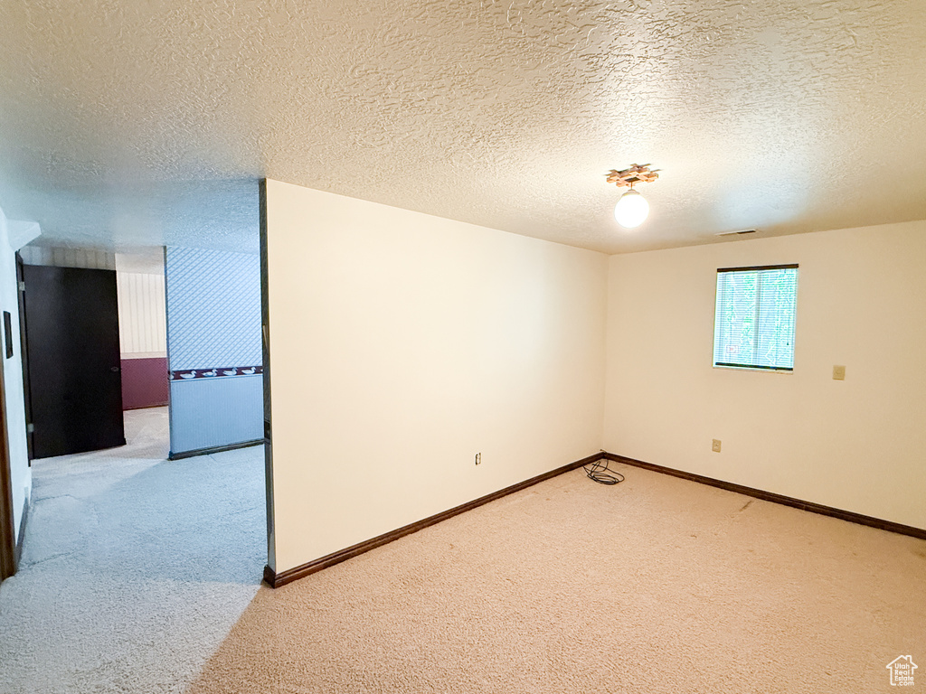 Unfurnished room with light carpet, a textured ceiling, and baseboards