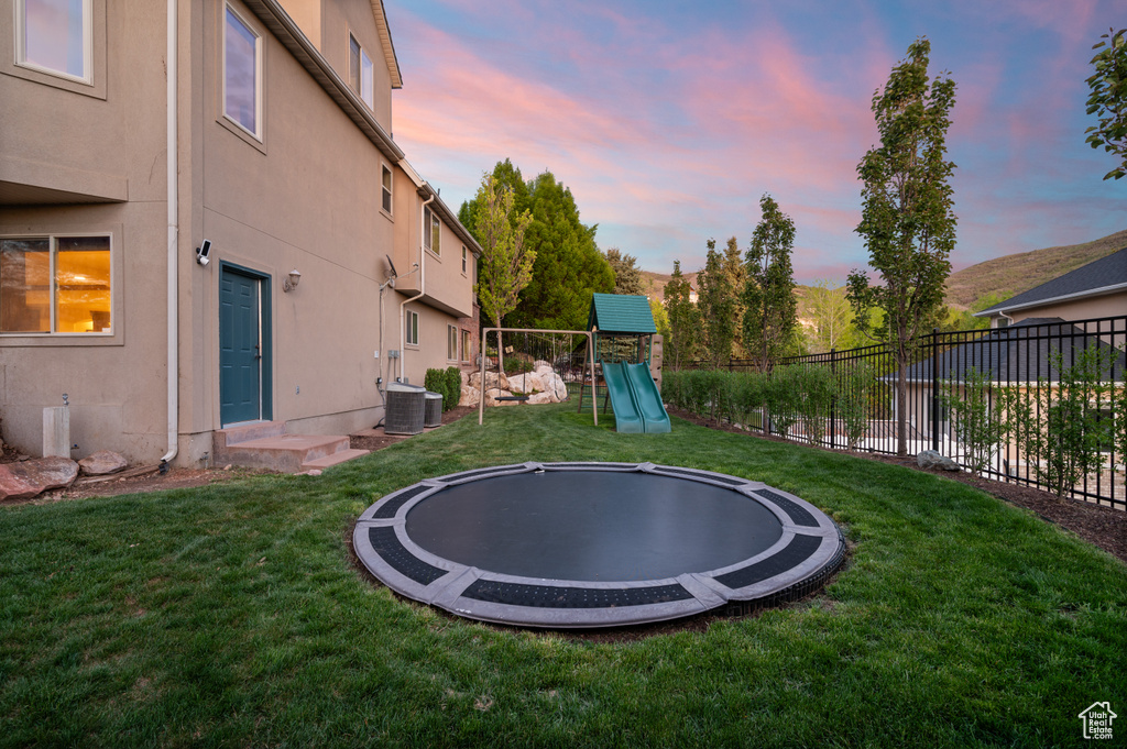 Yard at dusk featuring a trampoline and cooling unit