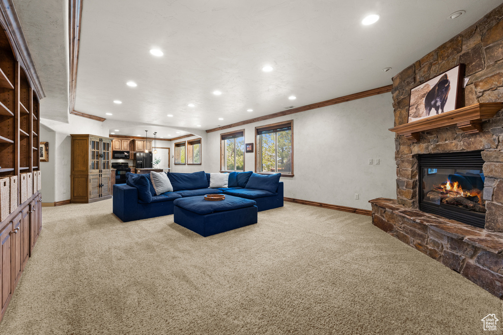 Living room with light carpet, crown molding, recessed lighting, a stone fireplace, and baseboards