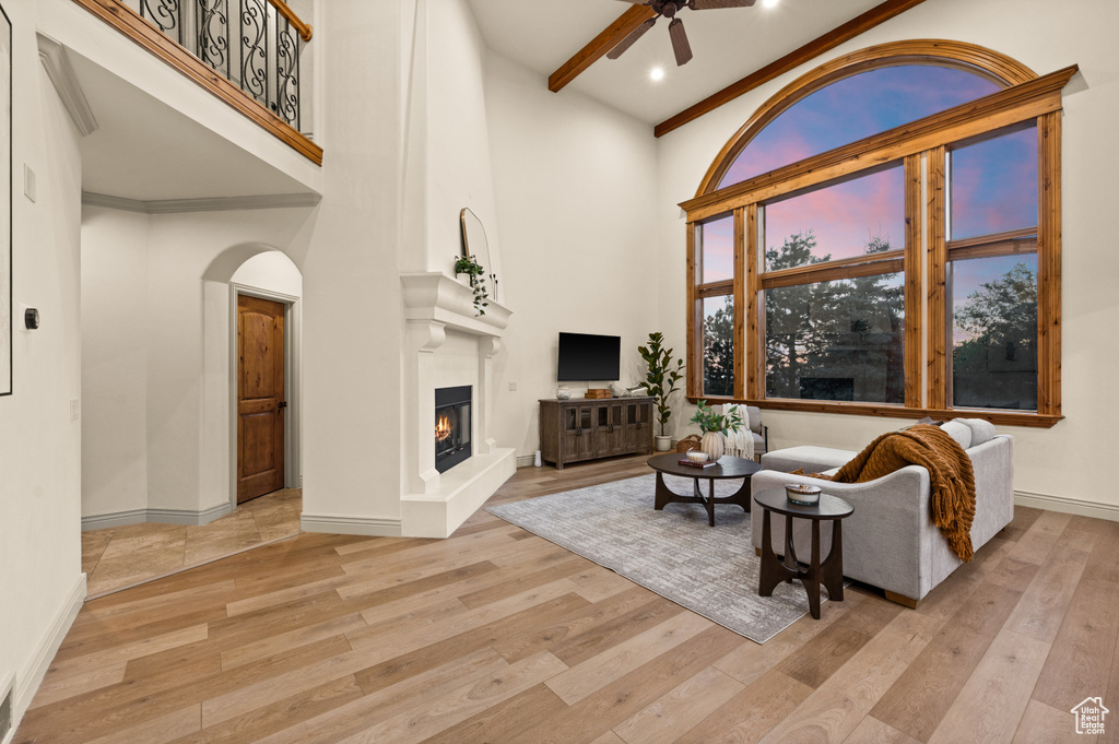 Living area featuring wood finished floors, ceiling fan, a large fireplace, baseboards, and a high ceiling