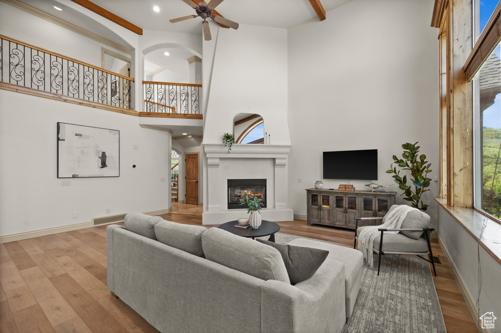 Living area with a high ceiling, a glass covered fireplace, wood finished floors, ceiling fan, and recessed lighting