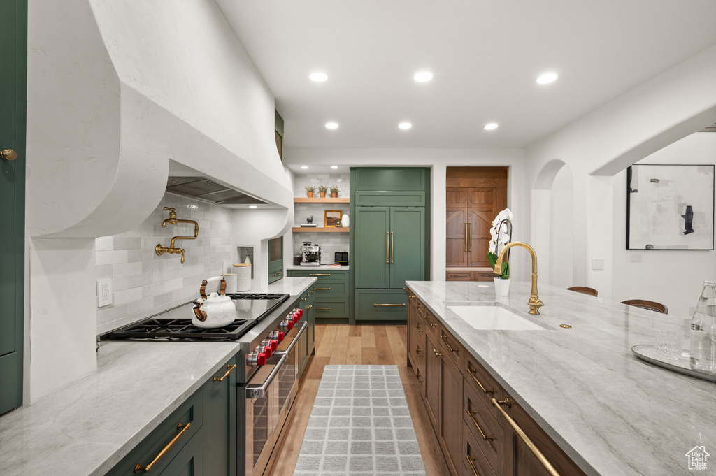 Kitchen featuring high quality appliances, a sink, green cabinets, recessed lighting, and decorative backsplash