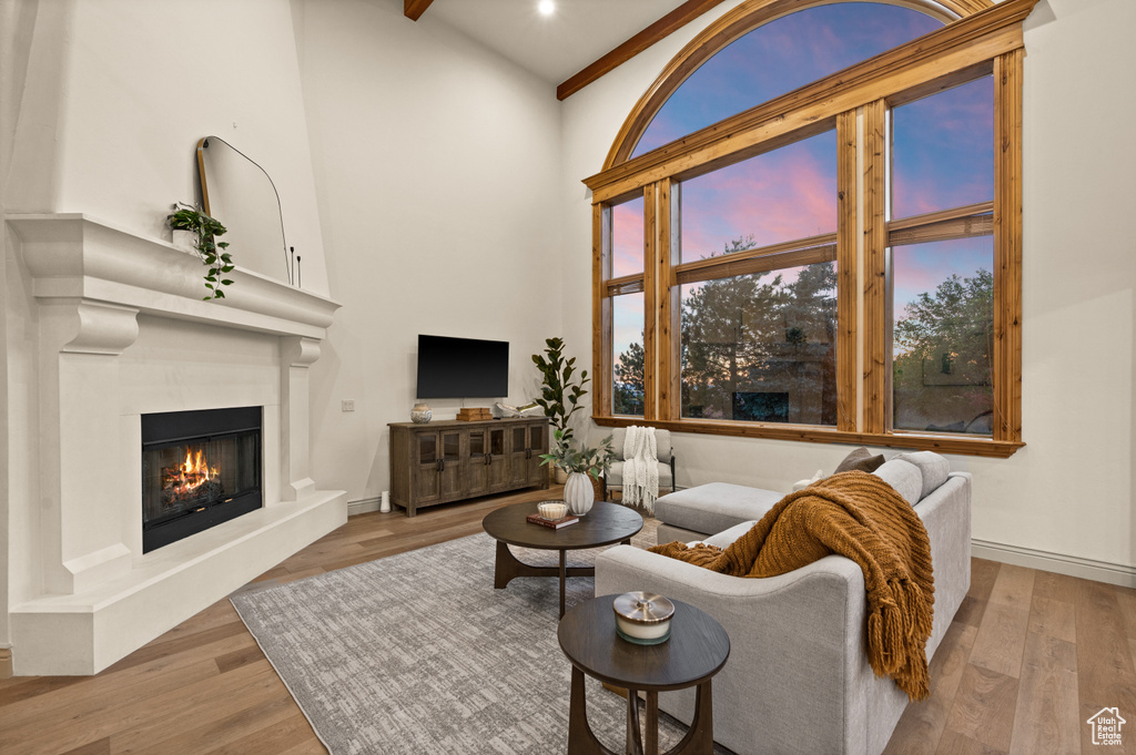 Living room with a towering ceiling, a glass covered fireplace, wood finished floors, beamed ceiling, and baseboards