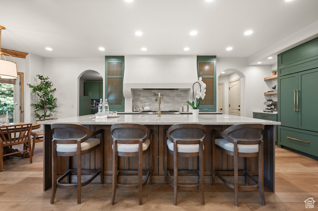 Kitchen featuring green cabinetry, arched walkways, backsplash, light stone counters, and recessed lighting