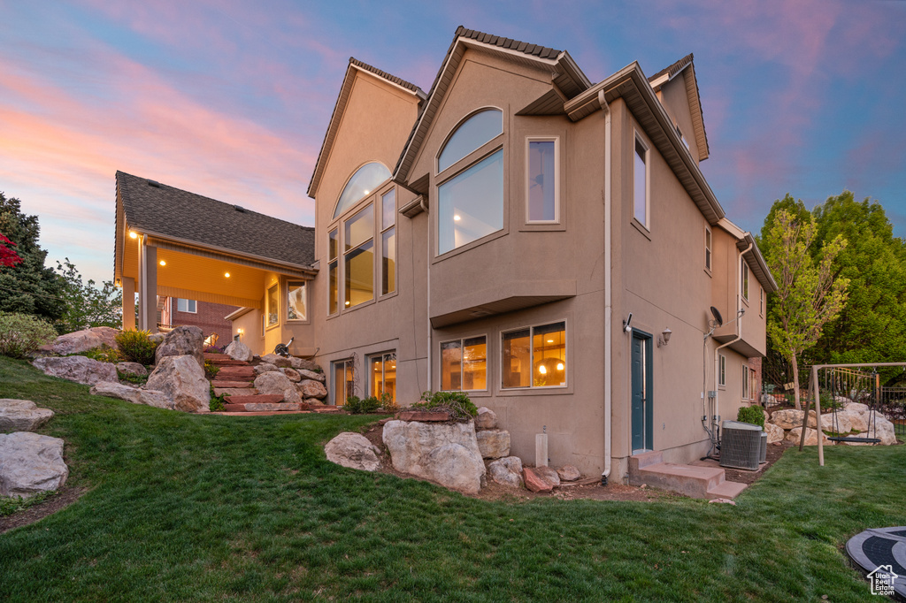 Rear view of property featuring a yard, stucco siding, and central AC unit