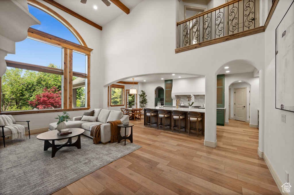 Living area with arched walkways, a towering ceiling, a ceiling fan, light wood-style flooring, and beam ceiling