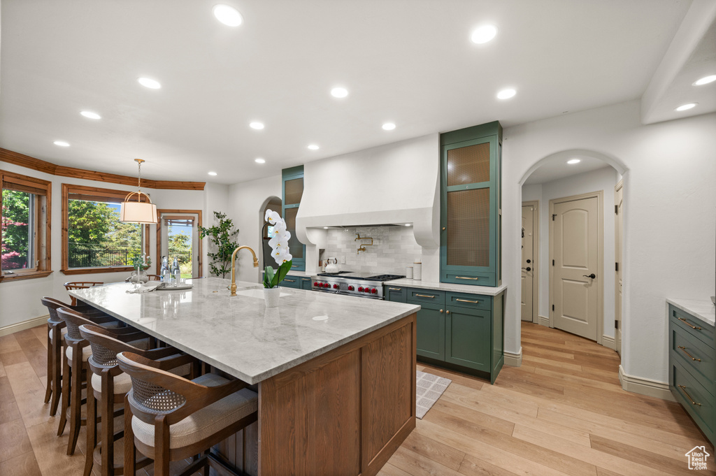 Kitchen featuring green cabinets, recessed lighting, decorative backsplash, arched walkways, and an island with sink