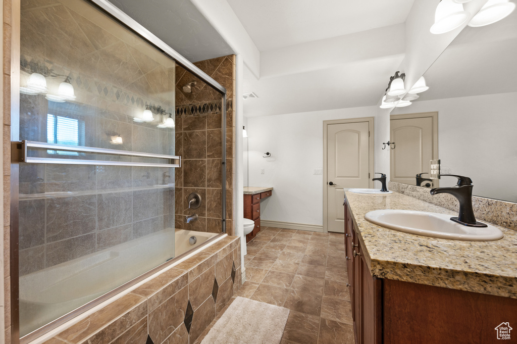 Bathroom with double vanity, toilet, tiled shower / bath combo, and baseboards