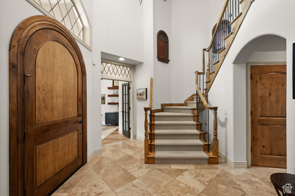 Entrance foyer featuring arched walkways, a high ceiling, stairway, baseboards, and stone tile flooring