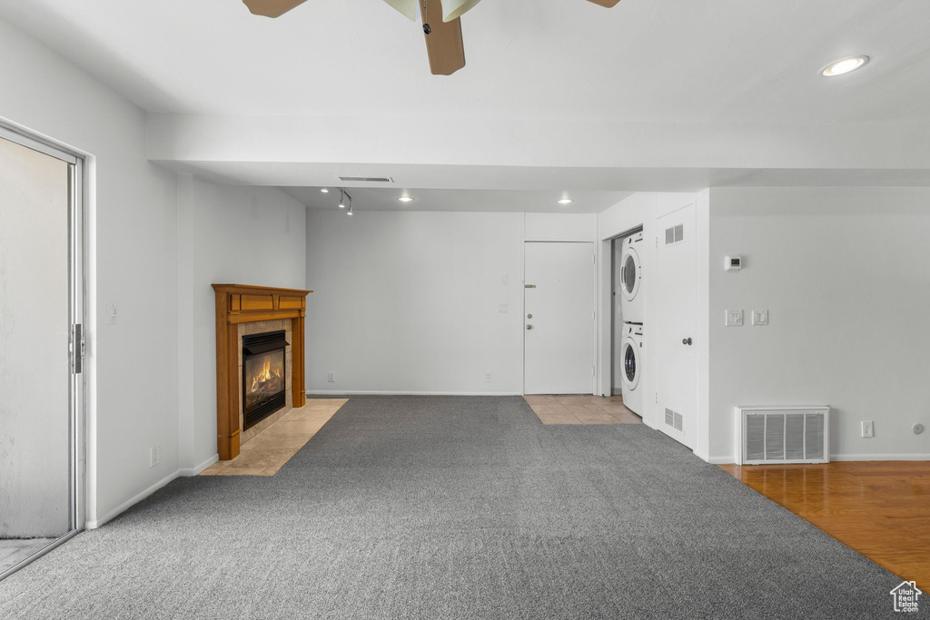 Unfurnished living room featuring stacked washer / drying machine, a ceiling fan, recessed lighting, a tiled fireplace, and baseboards