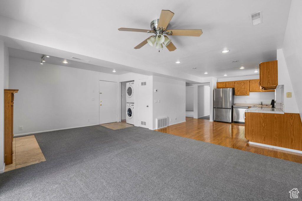Unfurnished living room featuring stacked washer / drying machine, recessed lighting, carpet floors, a ceiling fan, and baseboards