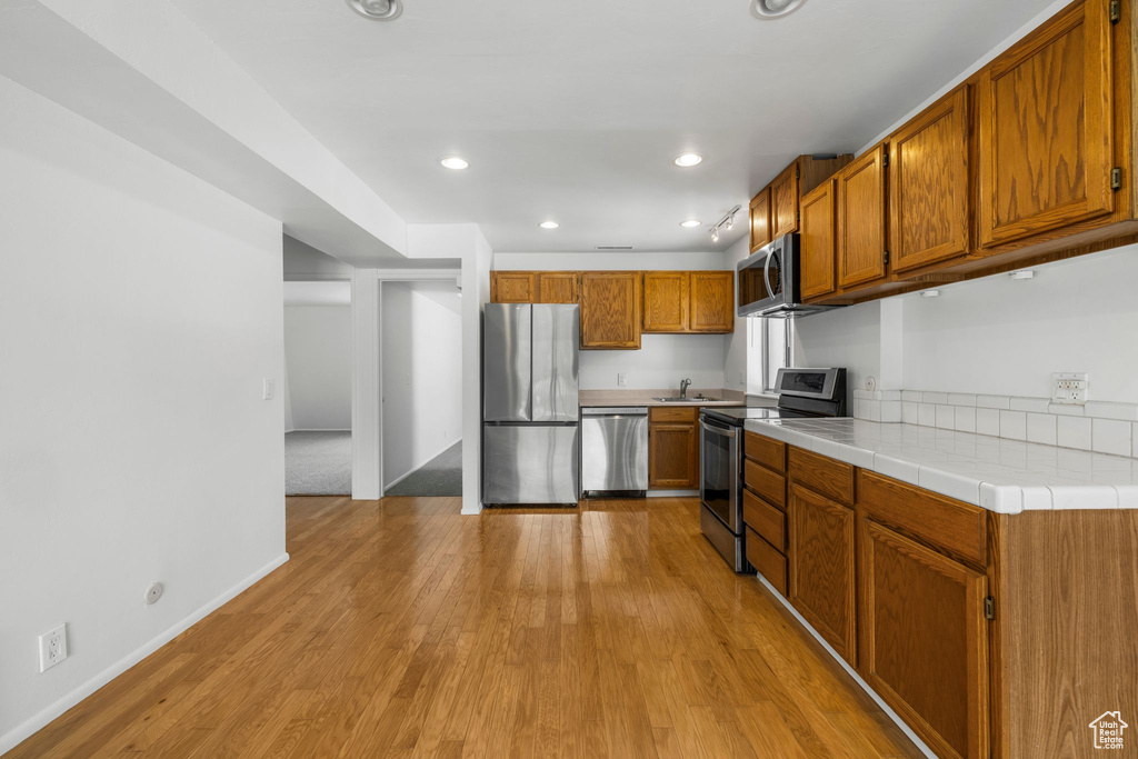 Kitchen with stainless steel appliances, brown cabinetry, light wood-style flooring, baseboards, and recessed lighting