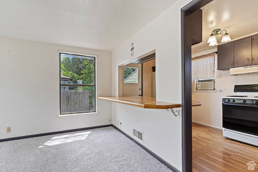 Kitchen with gas range, under cabinet range hood, baseboards, and an AC wall unit