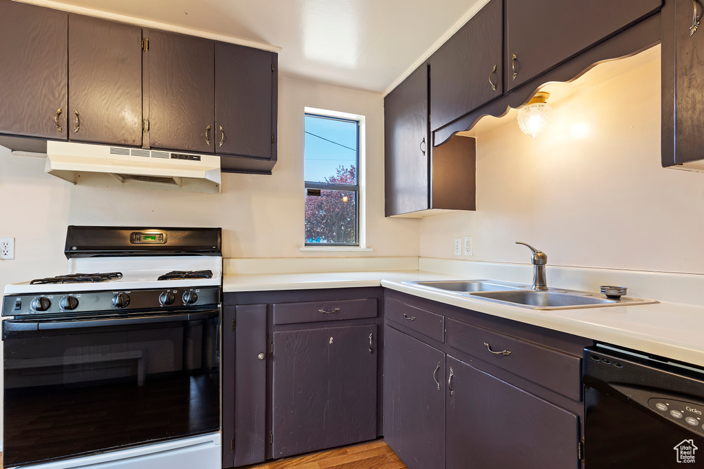Kitchen featuring range with gas stovetop, under cabinet range hood, dishwasher, a sink, and light countertops
