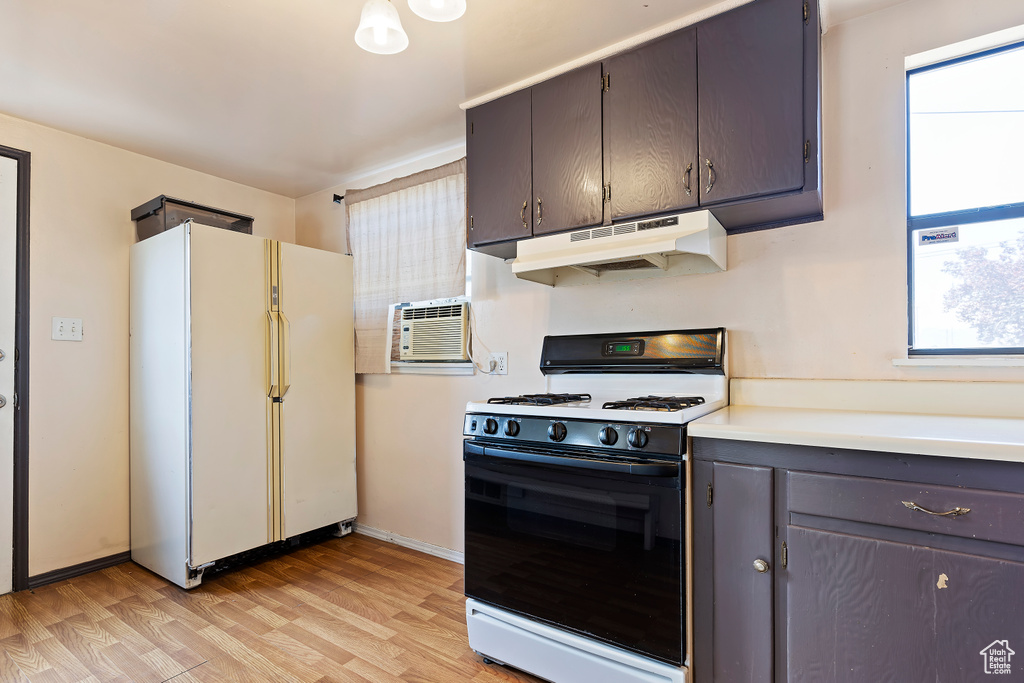 Kitchen with freestanding refrigerator, range with gas stovetop, under cabinet range hood, light wood finished floors, and light countertops