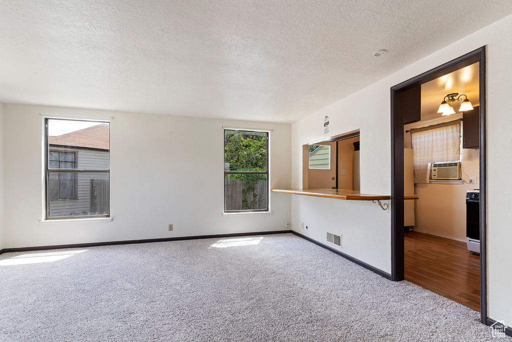 Carpeted spare room featuring a textured ceiling, baseboards, and cooling unit