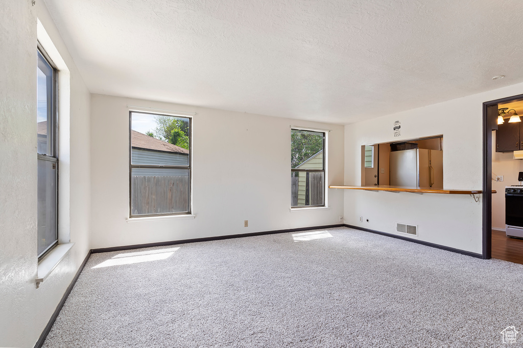 Carpeted spare room with plenty of natural light, baseboards, and a textured ceiling