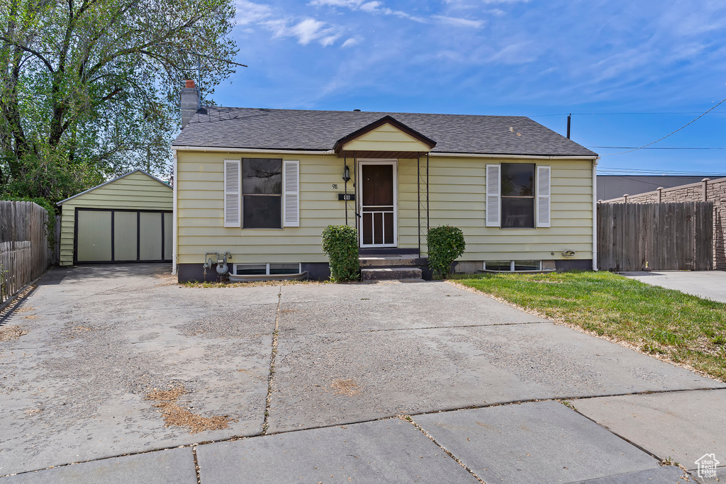 Bungalow-style house with an outdoor structure, fence, a garage, and a shingled roof