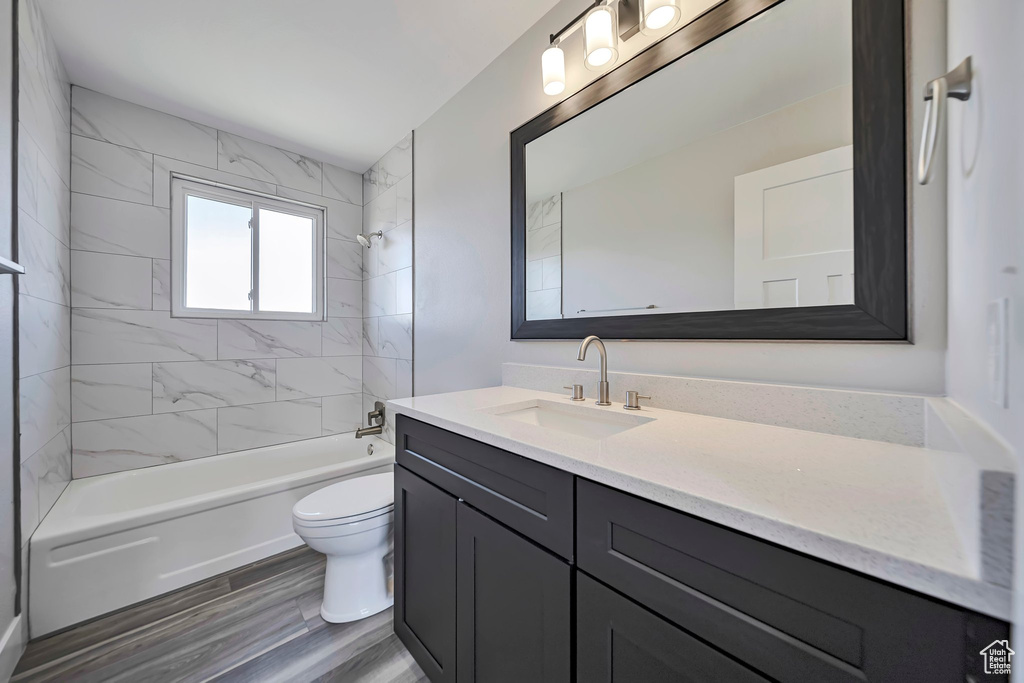 Bathroom featuring toilet, vanity, shower / bath combination, and wood finished floors