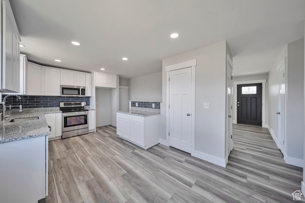 Kitchen featuring appliances with stainless steel finishes, a sink, tasteful backsplash, light wood-style floors, and recessed lighting